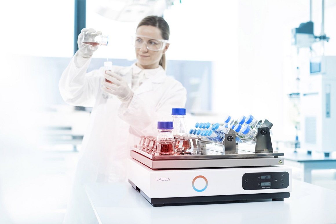 A laboratory worker stands behind a shaker and examines laboratory samples.