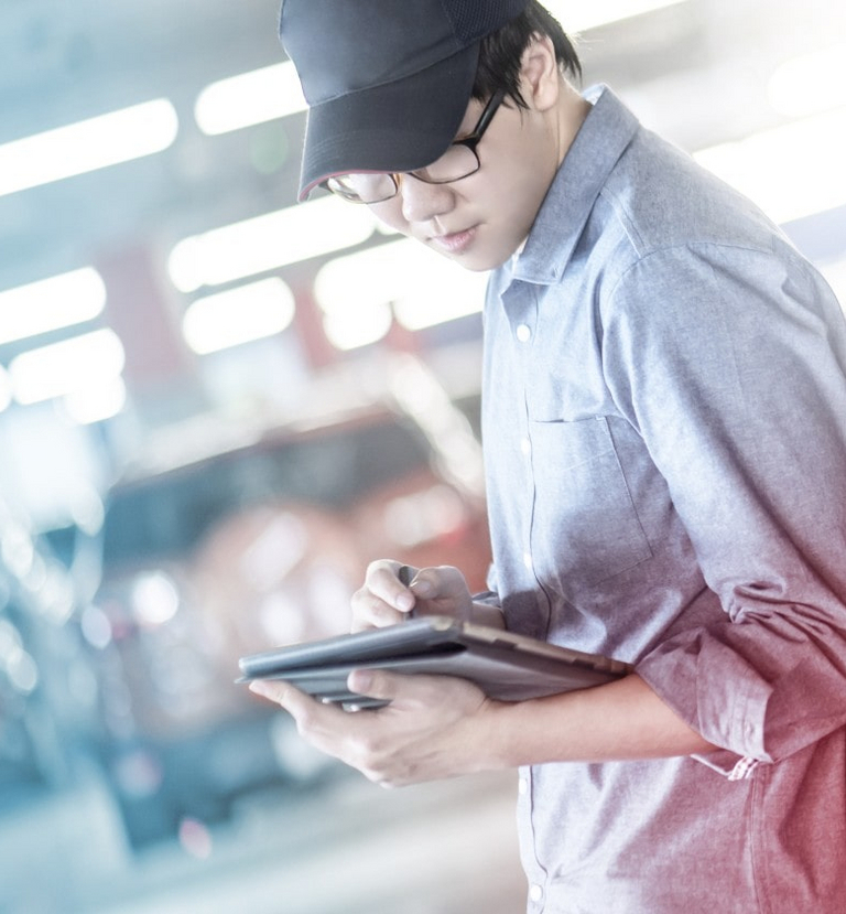 Une personne est appuyée contre une voiture dans un environnement d’usine et tient une tablette à la main.