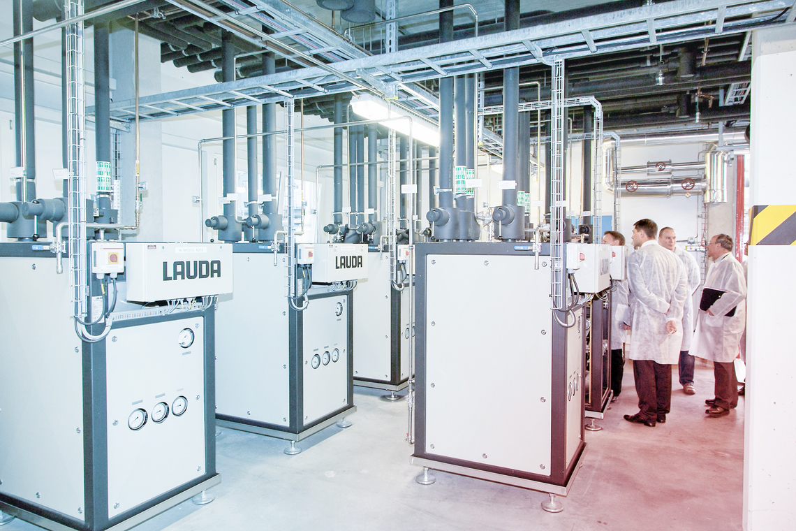 A group of people in white coats stands next to multiple secondary circuit units in an industrial room.
