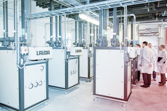 A group of people in white coats stands next to multiple secondary circuit units in an industrial room.